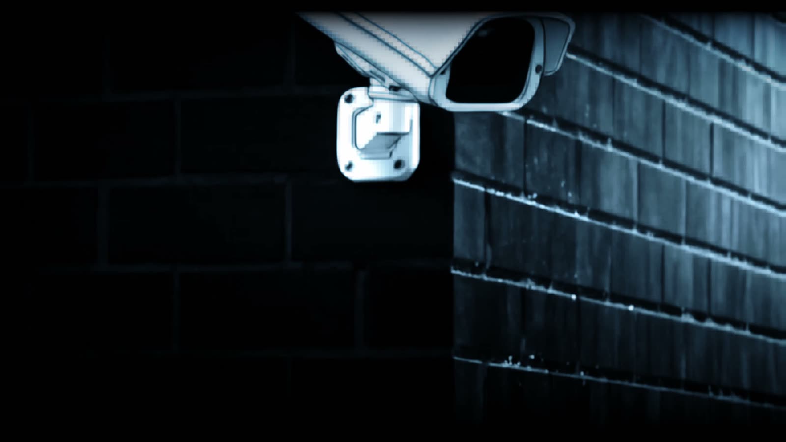 A security camera mounted on a dark brick wall, lit cold blue